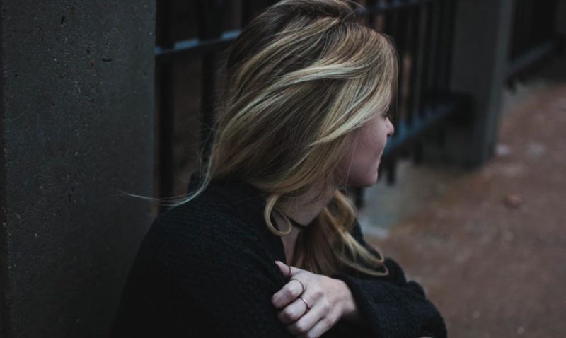 Girl looking away from camera with blonde hair in a dark street during the day