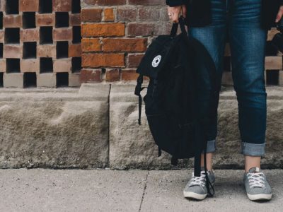 Student's legs wearing jeans holding black bag on street