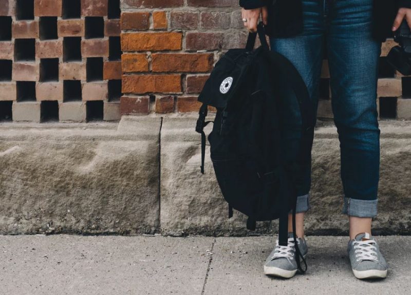 Student's legs wearing jeans holding black bag on street