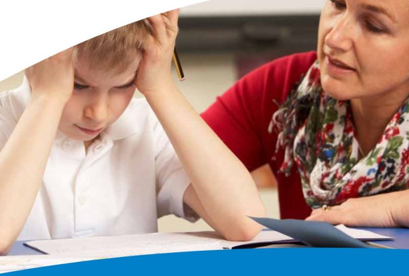 School child at desk with head in hands, female teacher looking concerned for him