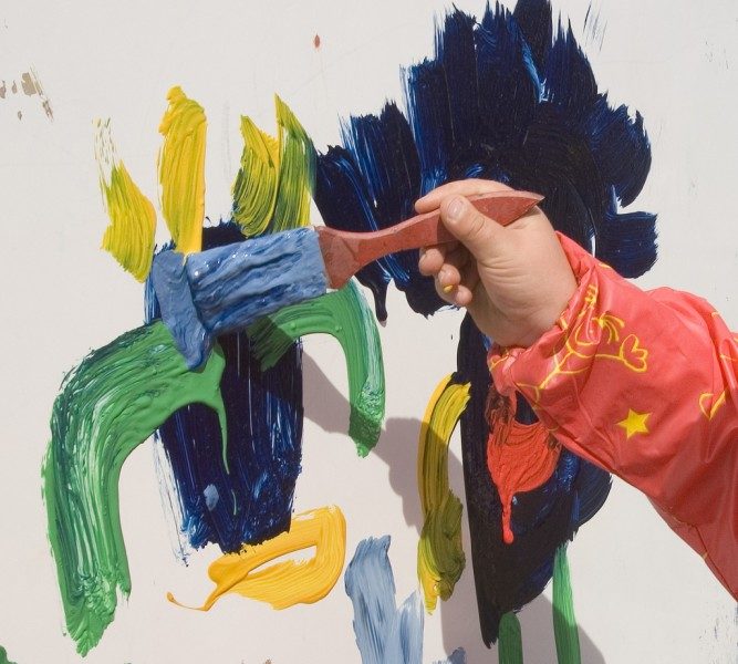 Child's hand painting on a wall with coloured paints