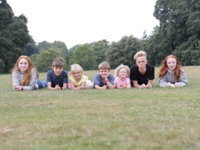 Seven Fostering Devon children - three teens and four school age -laying on grass facing towards the camera