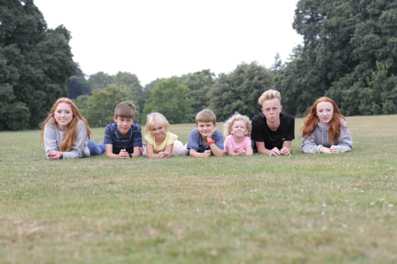 Seven Fostering Devon children - three teens and four school age -laying on grass facing towards the camera