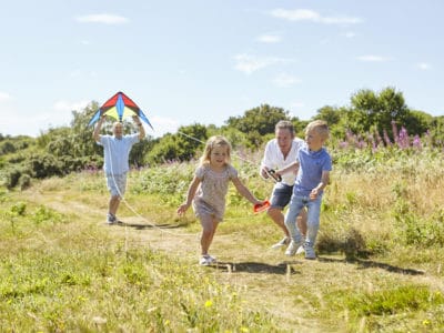 Adoptive male parents running with a kite and playing with their primary school age children on a Devon path, on a sunny day