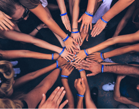 Looking down on a group of people in circle each with a hand placed into the middle