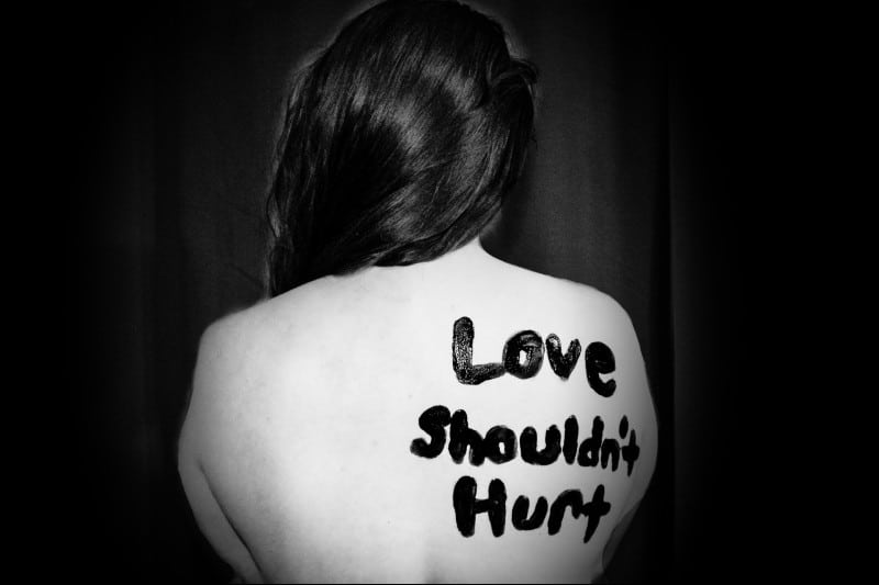 a woman with "love shouldn't hurt" written on here back