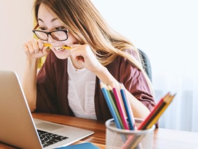 a student chewing nervously on a pencil while looking at a laptop