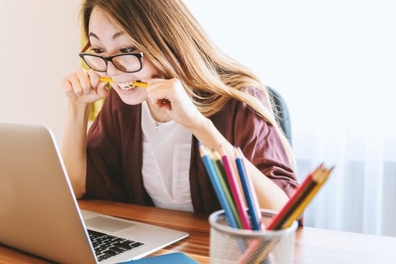 a student chewing nervously on a pencil while looking at a laptop