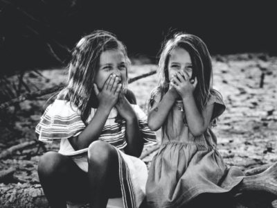 two sisters sat on a log smiling behind their hands