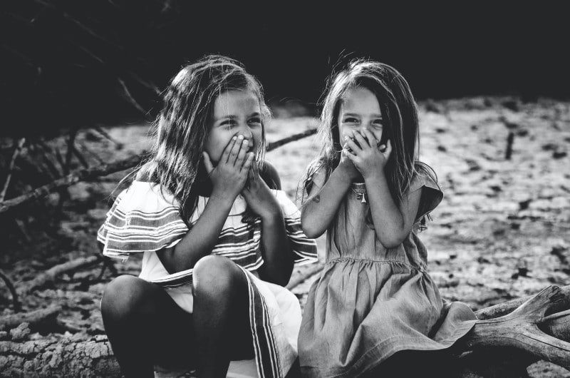 two sisters sat on a log smiling behind their hands