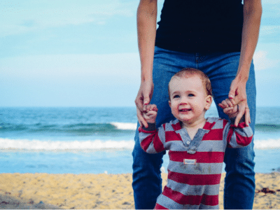 a father assisting his toddler to walk at the beach