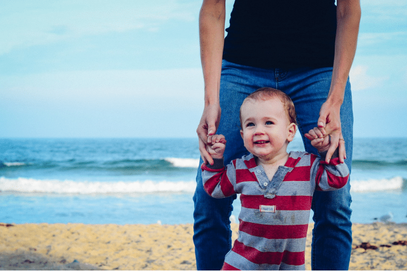 a father assisting his toddler to walk at the beach