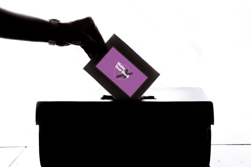 a hand placing a vote into a ballot box