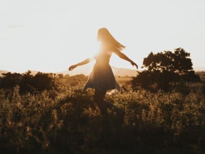 a woman skipping through a field at sunset