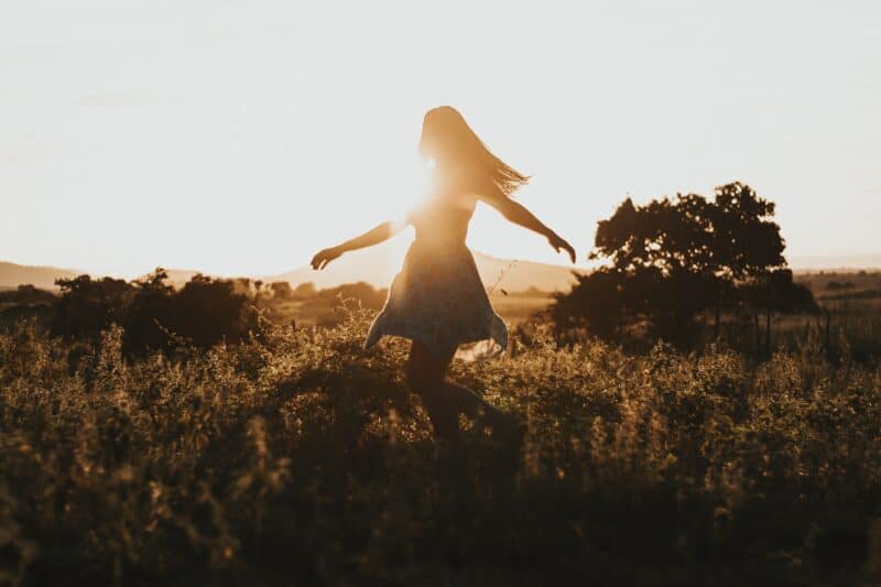 a woman skipping through a field at sunset